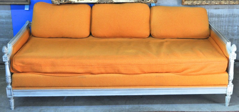 Een rustbed van witgepatineerd hout in Lodewijk XVI-stijl met oranje bekleding en drie kussens.