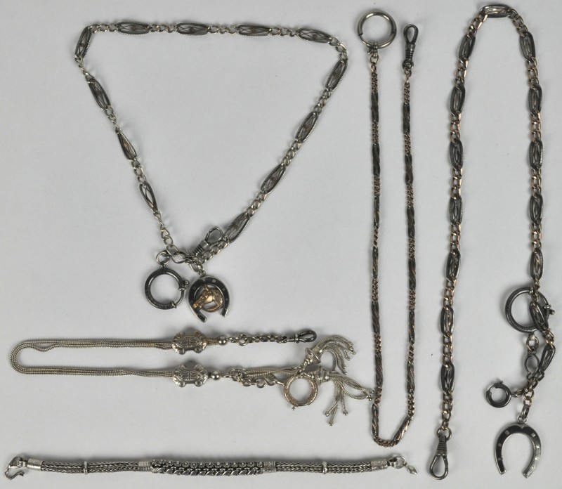 Vijf verschillende zilveren horlogekettingen, twee met hangers in de vorm van een hoefijzer.