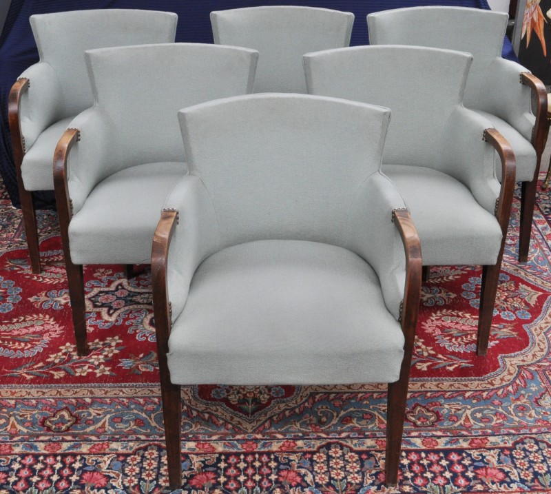 Een reeks van zes notenhouten fauteuils met stoffen bekleding.