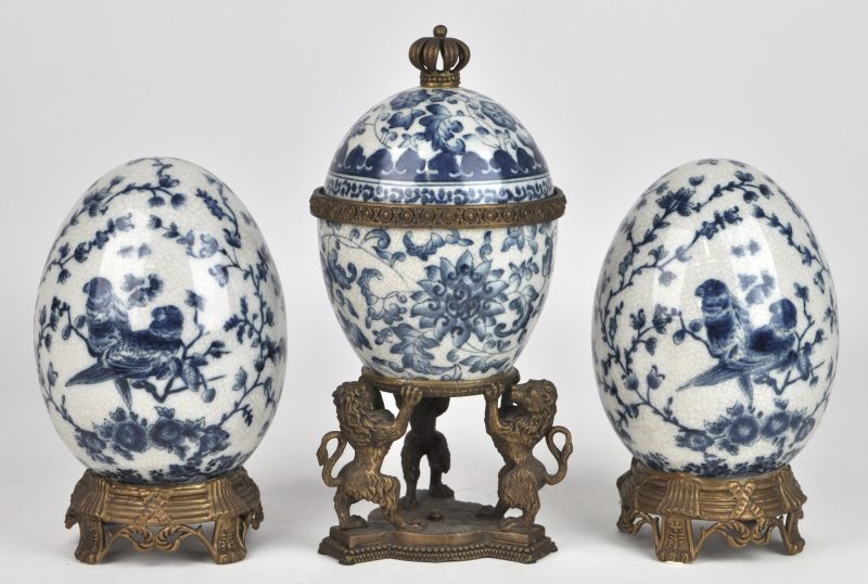 Een eivormige dekselpot van blauw en wit porselein, gedragen door drie heraldische leeuwen van brons. Onderaan gemerkt. We voegen er twee gelijkaardige eieren van blauw en wit porselein op koperen voet aan toe.
