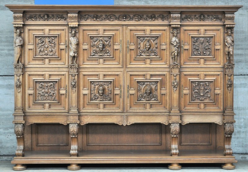 Een vierdeurscredenza van gesculpteerd eikenhout in renaissancestijl met onderaan vier laden, de stijlen versierd met personages in hoogreliëf en vier karakterkoppen op de middelste paneeldeuren.