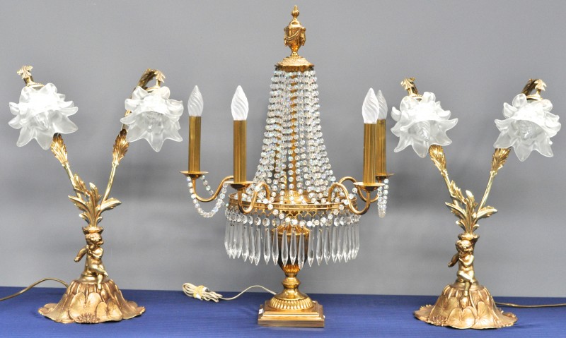 Twee lampen met twee lichtpunten van goudgepatineerd metaal in de vorm van bloemen met glazen kapjes en versierd met een putto op waterlelies. We voegen er een lamp in empirestijl aan toe.