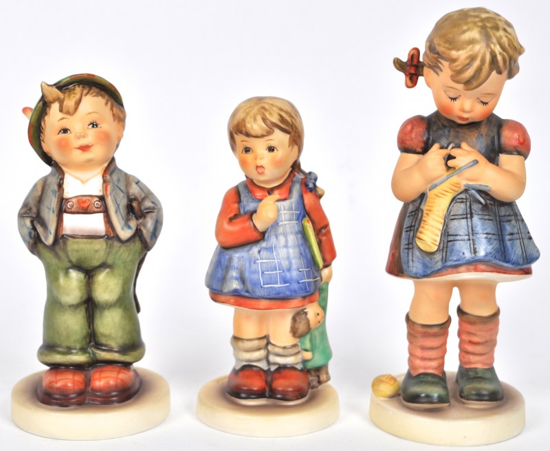 “Kleine Tiroler”, “Breiend meisje” & “Meisje met pop”. Drie beeldjes van meerkleurig porselein uit de reeks van M. I. Hummel.