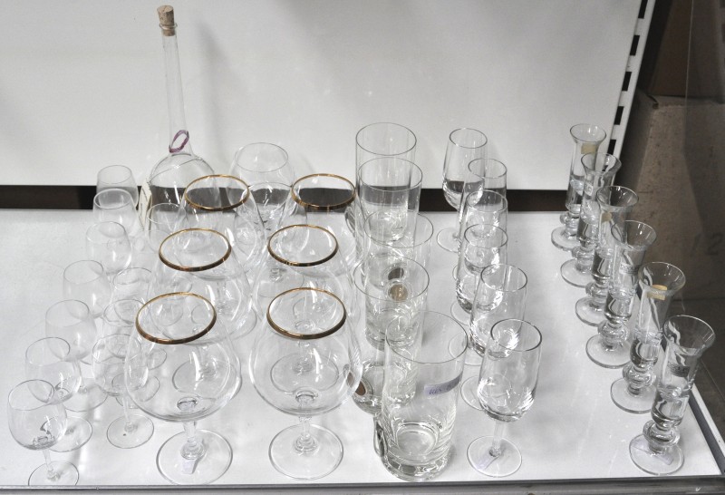 Een lot kristallen glazen, bestaande uit zes bierglazen, twaalf likeurglaasjes, een karaf, twee cognacglazen, vijf cocktailglazen met een ingewerkt muntstuk, zes sherryglazen en zes jeneverglaasjes.