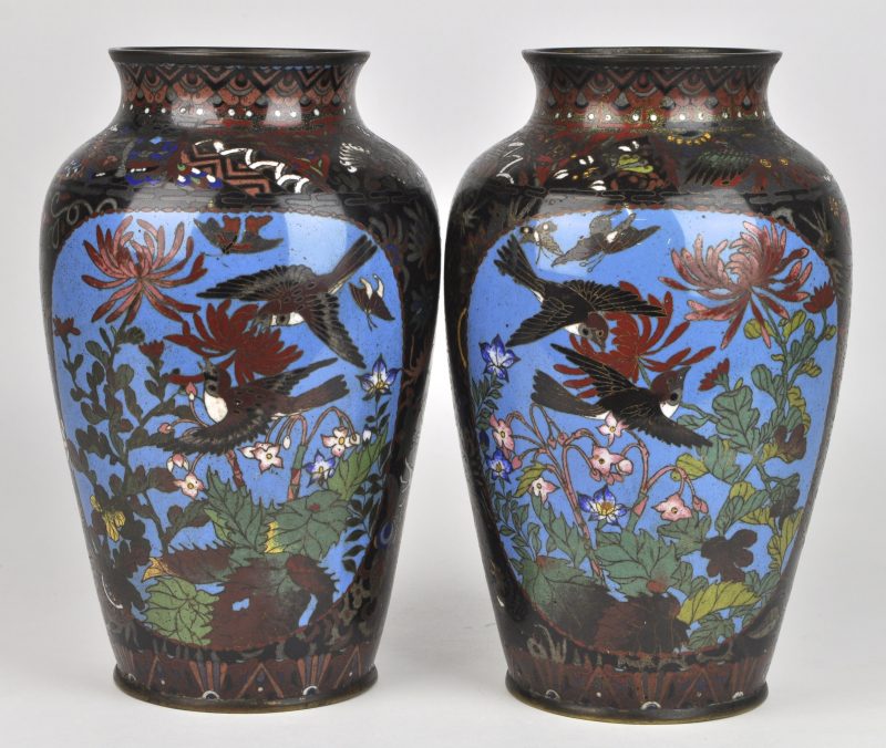 Een paar vazen van cloisonné op rood koper, versierd met een decor van bloemen, vlinders en vogels.