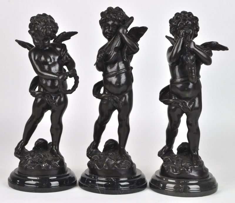 Drie musicerende engeltjes van donkergepatineerd brons op marmeren sokkels.
