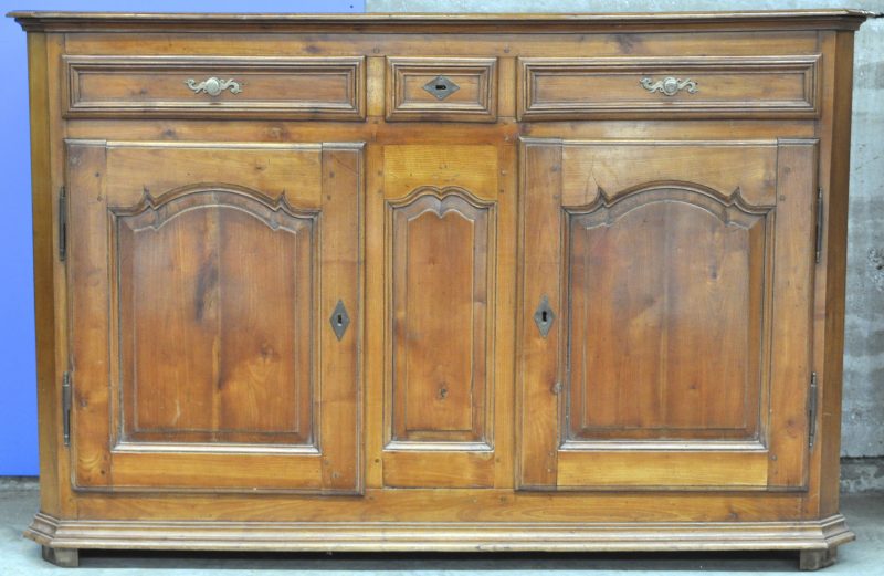 Een buffetkast van gesculpteerd hout met twee grote en een kleine lade boven twee gemoulureerde deuren.
