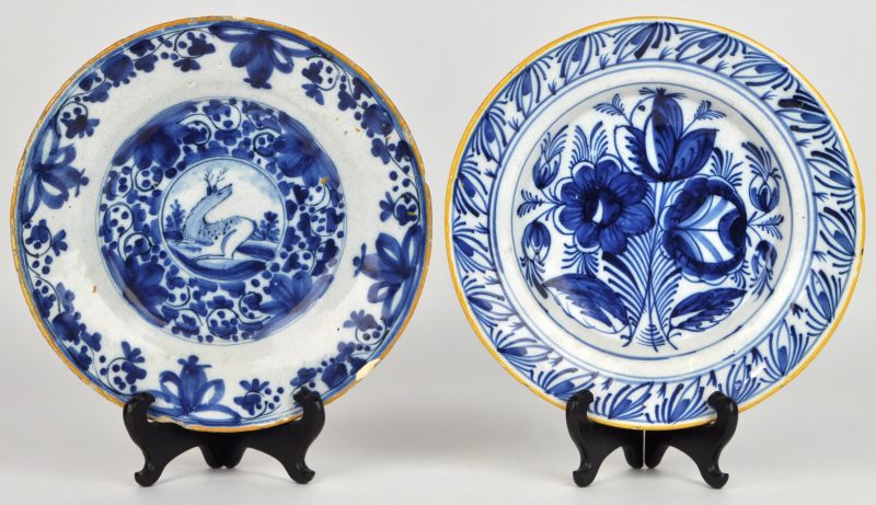 Een paar borden van blauw en wit aardewerk, waarvan één met een bloemendecor, het ander met een liggend hert op het plat en beiden met gele rand. Delft, XVIIIe eeuw.