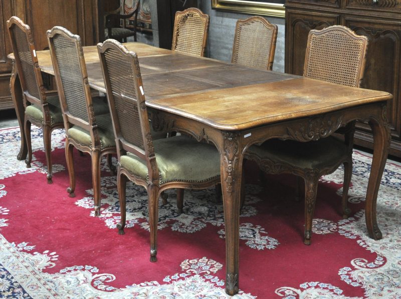Een eettafel van gesculpteerd eikenhout in Lodewijk XV-stijl met zes bijbehorende stoelen met gecanneerde rug. Schade aan het vlechtwerk.
