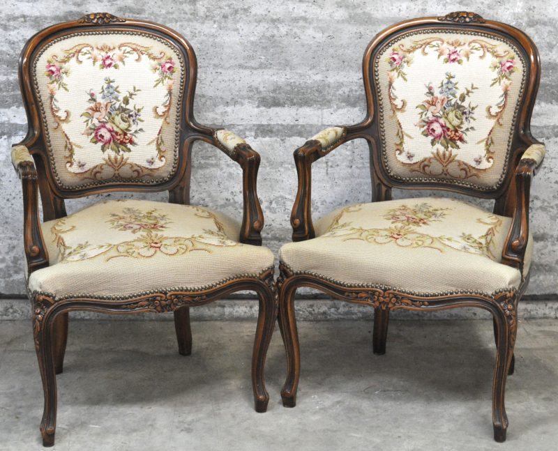 Twee fauteuils à la reine van gesculpteerd notenhout, bekleed met naaldwerk.