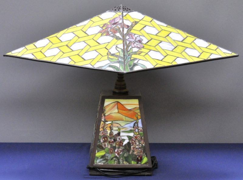 Een schemerlamp van brons met een kap van glas en lood en een lampenvoet, versierd met landschapsdecors van glasmozaïek.