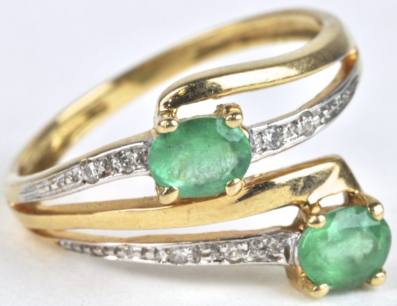 Een 18 karaats geel gouden ring bezet met briljanten met een gezamenlijk gewicht van ± 0,10 ct. en twee smaragden met een gezamenlijk gewicht van ± 0,50 ct.