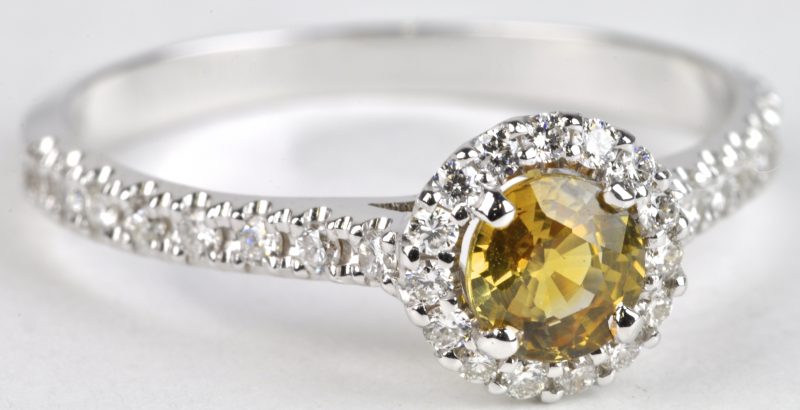 Een 18 karaats wit gouden ring bezet met diamanten met een gezamenlijk gewicht van ± 0,25 ct en een centrale gele saffier van ± 0,54 ct.