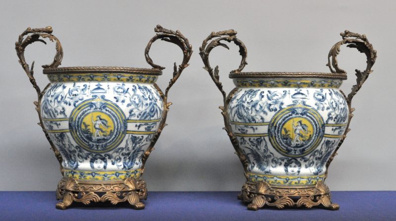 Twee barokke cachepots van meerkleurig aardewerk met een decor van mythologische figuren en versierd met bronzen monturen. Onderaan gemerkt.