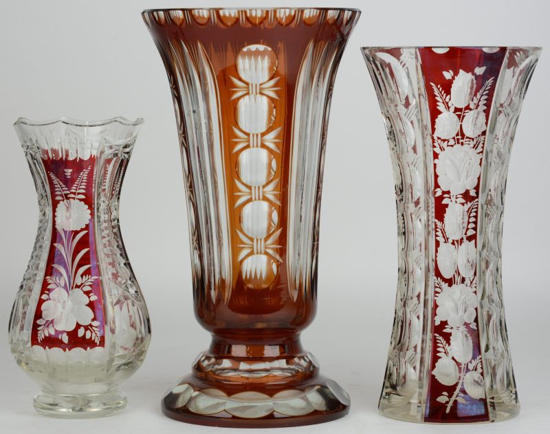 Drie vazen in diverse uitvoeringen van geslepen Boheems kristal en rood gekleurd in de massa.