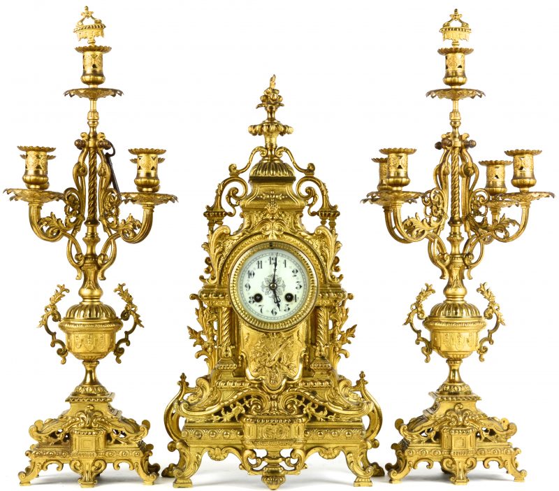 Een driedelig klokstel van geel koper, bestaande uit een pendule en twee kandelaars in neo-barokstijl.
