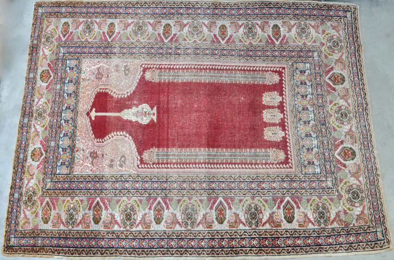 Een handgeknoopt Oosters tapijt met een centrale mirhab. Slijtage.