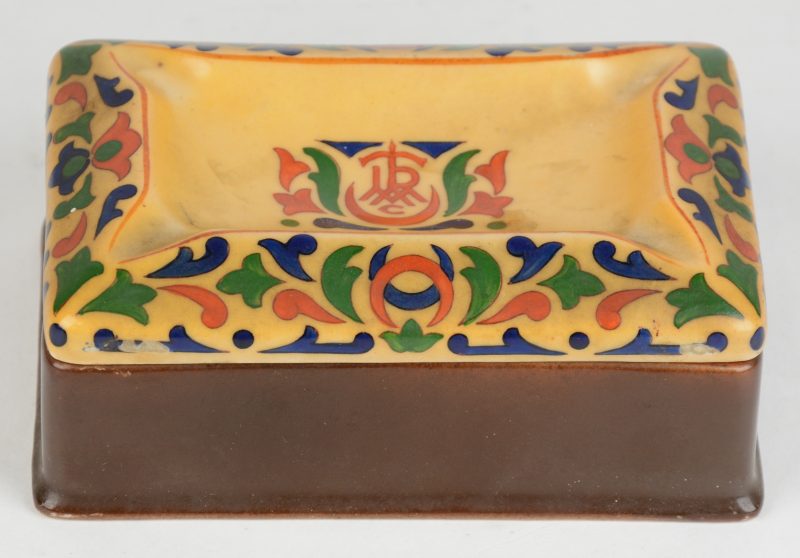 Een sigarettendoos van meerkleurig porselein met het deksel in de vorm van een asbak. Onderaan gemerkt. Nederland, jaren ‘20.
