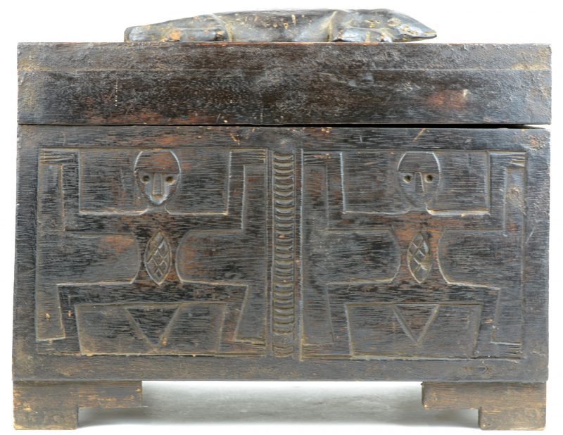 Een Afrikaans kistje van gesculpteerd hardhout, versierd met figuren in reliëf en bovenaan getooid met een hagedis.