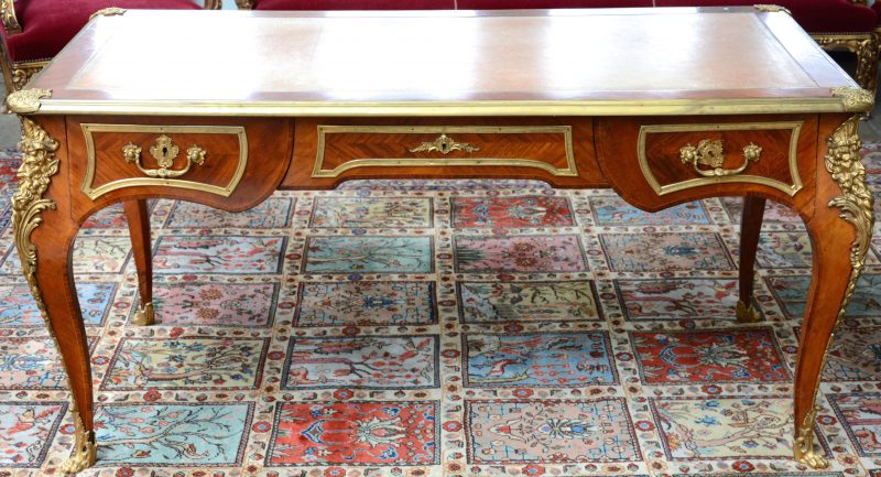 Een bureau van gefineerd hout in Lodewijk XV-stijl met drie laden, een gevacheteerd blad en versierd met bronsbeslag.