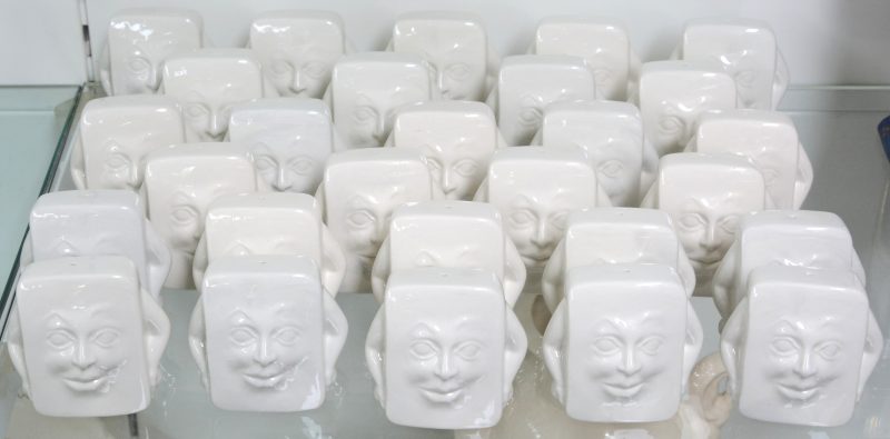 Een partij  rechthoekige zoutvaatjes van monochroom wit aardewerk met een gezicht in reliëf en armen.