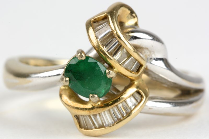 Een 18 karaats wit en geel gouden ring bezet met diamantbaguetten met een gezamenlijk gewicht van ± 0,40 ct. en een smaragd van ± 0,20 ct.