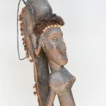 Een houten Afrikaans fetisjbeeld op een ijzeren sokkel.