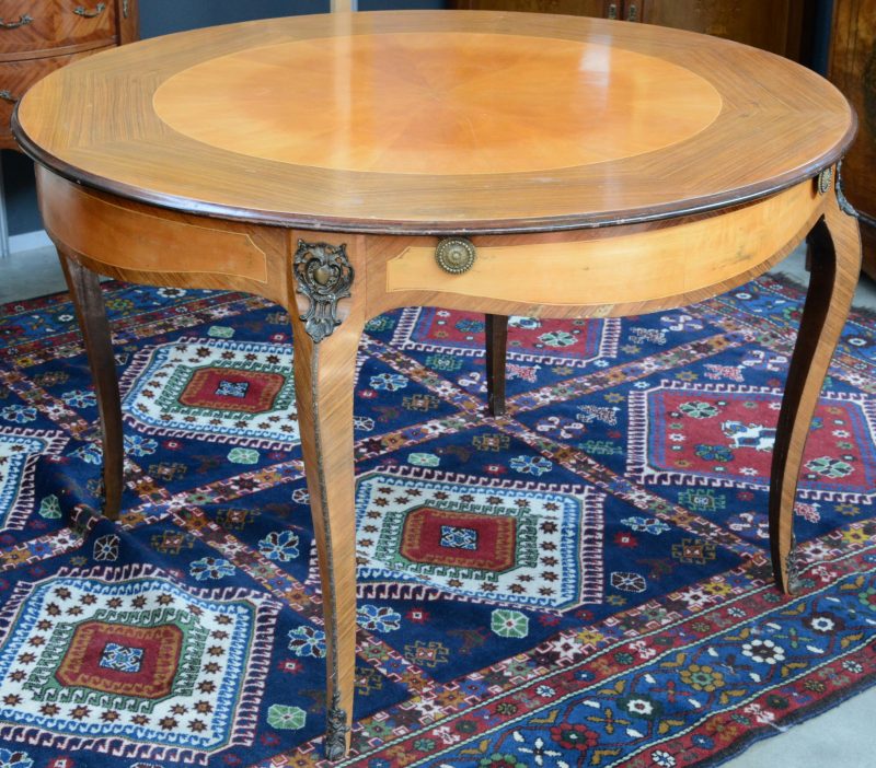 Een ronde tafel van gefineerd hout in Lodewijk XV-stijl. Vier gebogen poten met bronzen monturen.