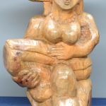 Een houten beeldhouwwerk van een zittende vrouw. Op een vierkante piëdestal van gefineerd hout. Gemonogrammeerd D.A. 1979.