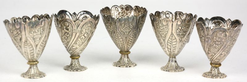 Vijf zilveren eierdopjes met een barok decor van bloemen.