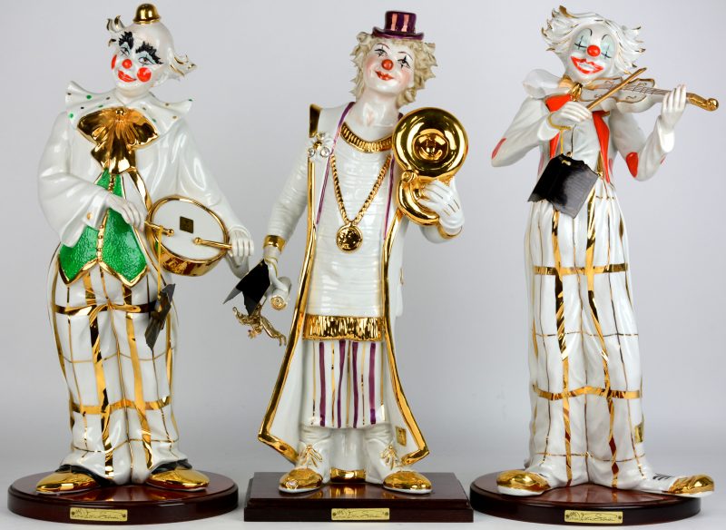 Een reeks van drie verschillende musicerende clowns van meerkleurig en verguld porselein. Italiaans werk.