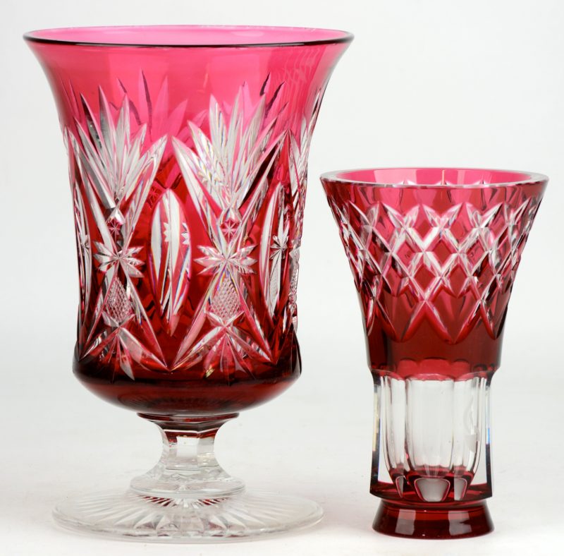 Een vaas op voet en een klein vaasje van geslepen kristal, rood gekleurd in de massa. Het tweede gemerkt van Val St. Lambert en met het logo van de Rijkswacht.