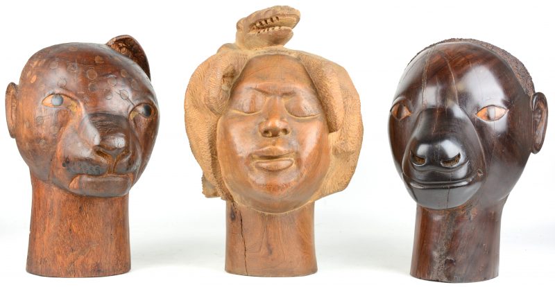 Drie gebeeldhouwde hoofden: een vrouw met een krokodil op het hoofd, een luipaard en een half luipaard-half man. Onderaan gemerkt. Bagamoyo, Tanzanië.