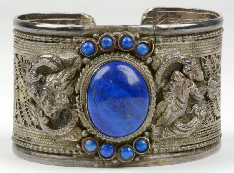 Een zilveren armband, versierd met ajourwerk en een centrale Lapis Lazuli, omringd met twee maal vier kleine exemplaartjes. 925‰.