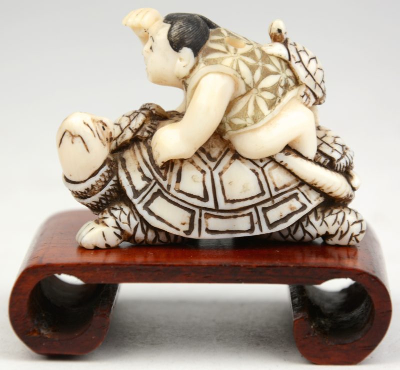 “Japans rijder op schildpad”. Een netsuke van gesculpteerd ivoor. Onderaan gesigneerd. Op houten voetstukje.