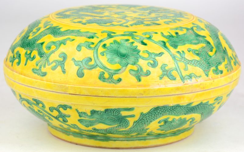 Een dekseldoos van Chinees porselein met een groen decor van draken en bloemen op een gele fond. Onderaan gemerkt.
