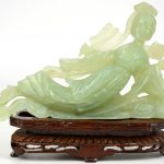 Een liggende Guan yin van gesculpteerd jade op houten sokkel en een balustervaas van Cantonporselein.