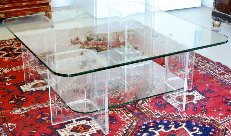 Een salontafel met vier plexiglazen poten en twee glazen bladen.