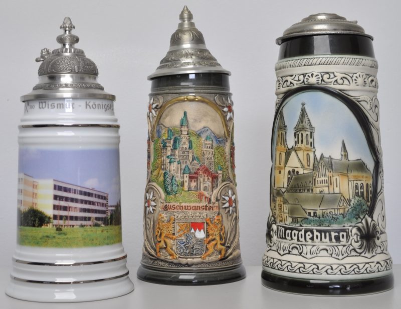 Drie bierpullen van aardewerk en porselein met tinnen deksels. Een met afbeelding van Neuschwanstein, één met Magdeburg, gemerkt Thüringer Manufaktur-Porzellan en één met Wismut-Königstein.