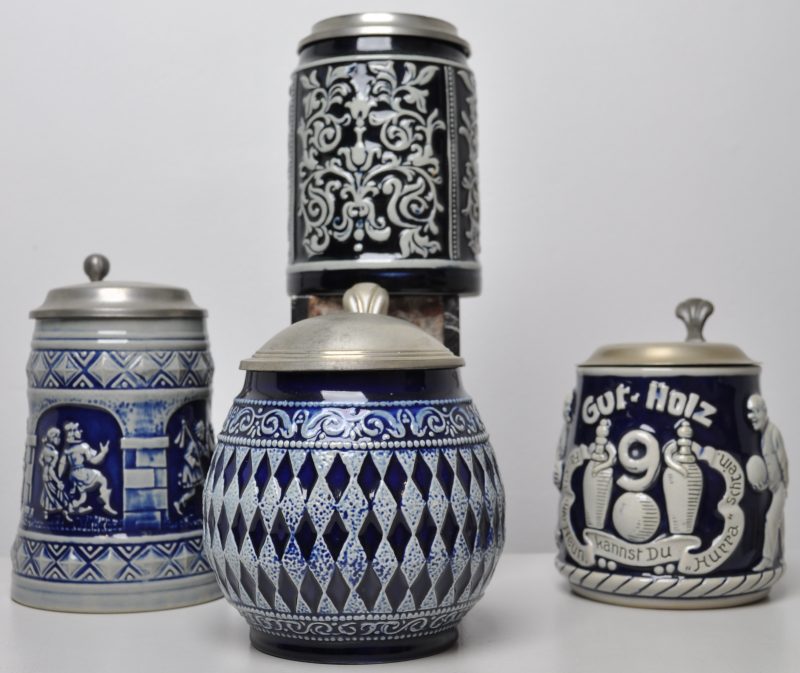 Vier bierpullen van blauw en grijs steengoed met tinnen deksels. Eén met guirlandes en met het logo van Pelikan op het deksel (H. 15 cm).  Eén met dansers, onderaan gemerkt (H. 16,5 cm). Eén bolle met ruitmotief (H. 15 cm). Eén met kegelaars “Gut-Holz”, onderaan gemerkt (H. 14 cm).