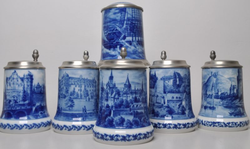 Zes bierpullen van porselein met tinnen deksels. Vijf in blauw en wit versierd met Duitse kastelen, onderaan gemerkt Berlin Genuine Blue China, Jahresseidel 1975, 1980, 1982, 1990 en 2000 (H. 17 cm). Eén met hetzelfde merk maar “Nautica 1979” (H. 17 cm).