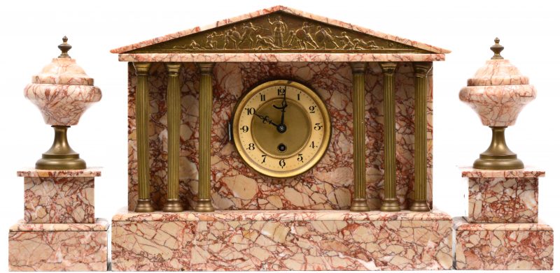 Een driedelig klokstel van roze marmer met de pendule in de vorm van een Griekse tempel met koperen zuiltjes en fronton.