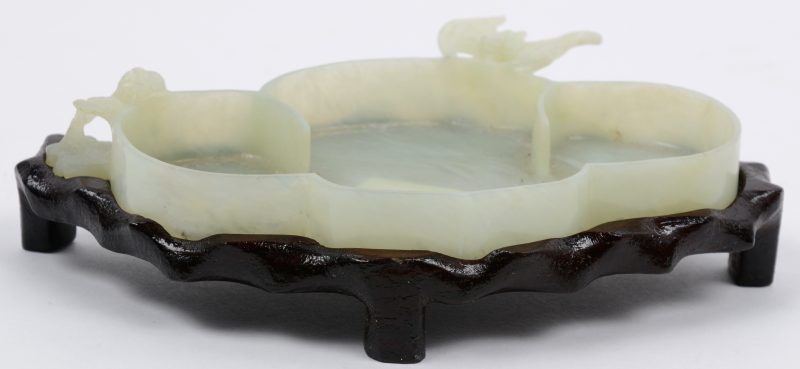 Een waterschaaltje van gesculpteerd jade, versierd met een vleermuis. Op een houten sokkeltje.