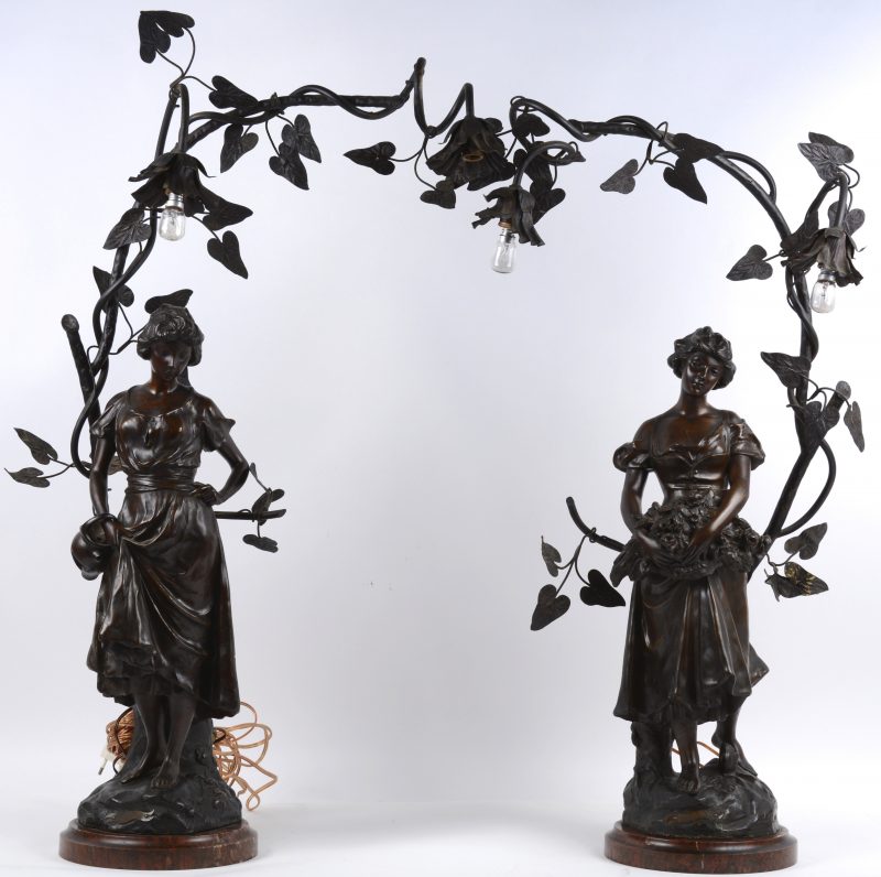 Een paar lapen van zamak met twee lichtpunten in de vorm van bloemenranken, telkens gedragen door een vrouwenfiguur, de eerste met een bloemenmand en de andere met een kruik. Op marmeren voetstukken. Omstreeks 1900.