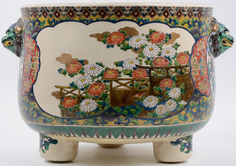 Een cachepot van meerkleurig Japans aardewerk op drie voetjes met pauwen en bloemen n het decor en met twee Fohondkoppen als handvatten.