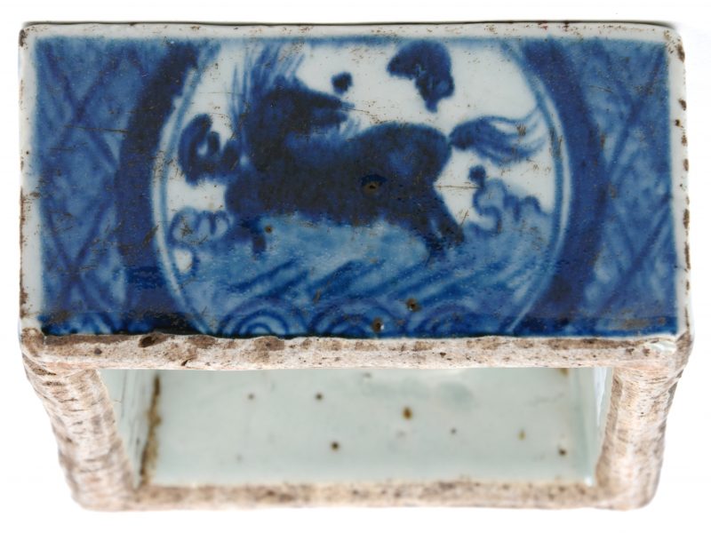Een vierkante inktpot van Chinees porselein met een blauw en wit decor van paarden en vissen en onderaan met Chinese tekens. Naar voorbeeld uit de Mingperiode.