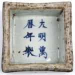 Een vierkante inktpot van Chinees porselein met een blauw en wit decor van paarden en vissen en onderaan met Chinese tekens. Naar voorbeeld uit de Mingperiode.