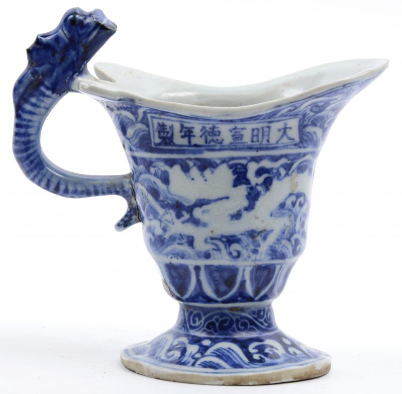 Een schenkkannetje van blauw en wit Chinees porselein met het handvat in de vorm van een draak.