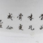 Een kleine cachepot van Chinees porselein met een meerkleurig decor van negen en zeven perzikken en Chinese tekens achteraan.