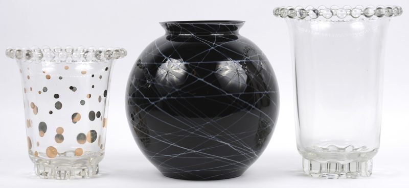 Een lot glaswerk, bestaande uit twee kleurloze vazen, waarvan één met verglde stippen en een bolle vaas van zwart glas met een grijs decor.